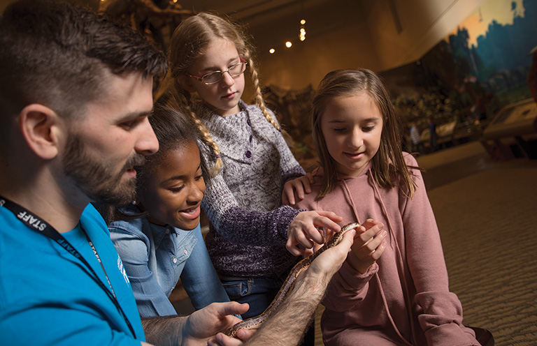 A museum educator showing a small snake to a group of children.