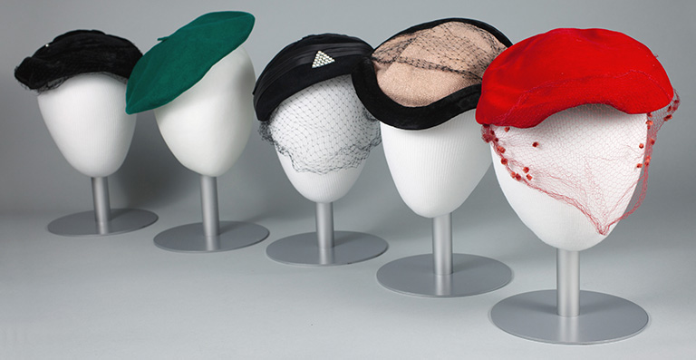 Five styrofoam heads displaying a selection of Julia Warhola’s hats.