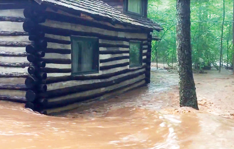 Muddy flood water rushing past a log cabin.