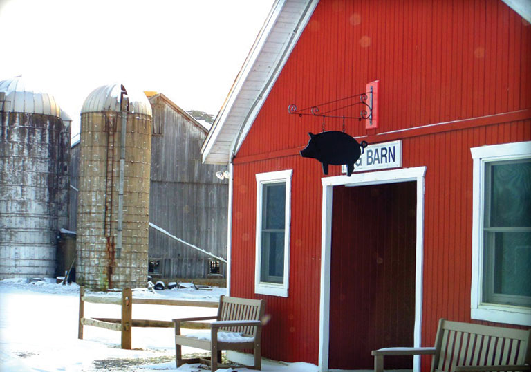 A red barn with a metal pig ornament hanging over the door.