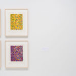 Installation view of an art exhibit with 6 colorful artworks hanging in rows.