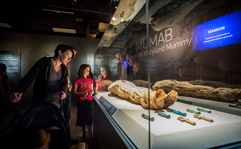 A family looking at a mummified body in an exhibit case.