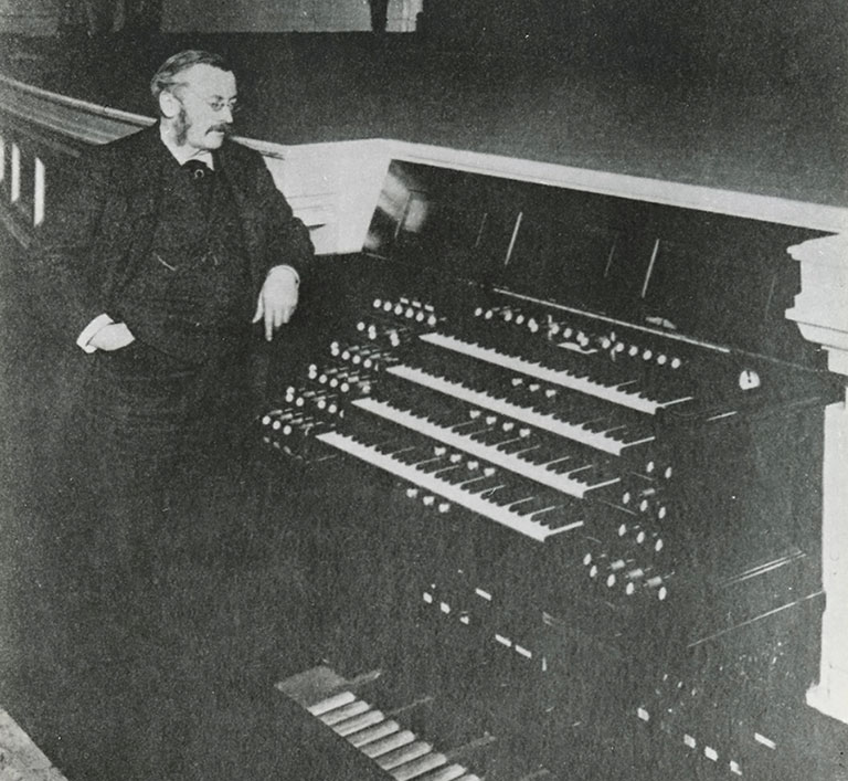 A vintage photograph of a man standing next to a pipe organ