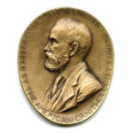 A gold medal with the profile of a bearded man.