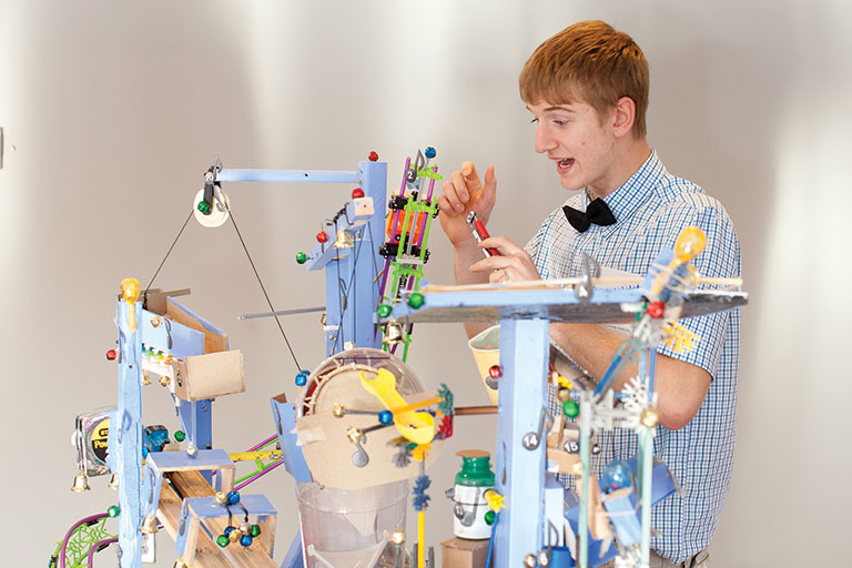 A teen boy working on a colorful contraption.