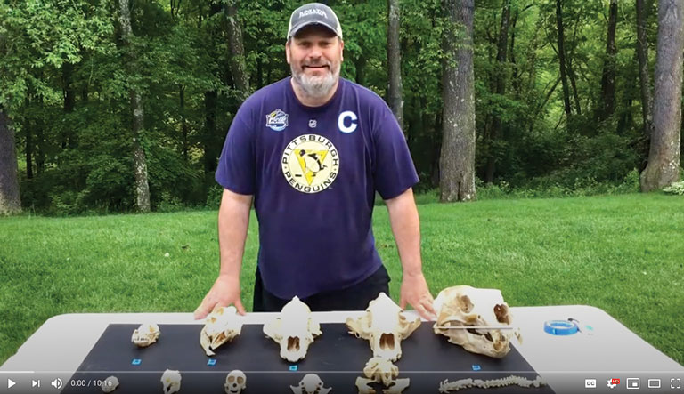 Christian Shane teaching a virtual class from outdoors. A collection of animal skulls is displayed on a table in front of him.