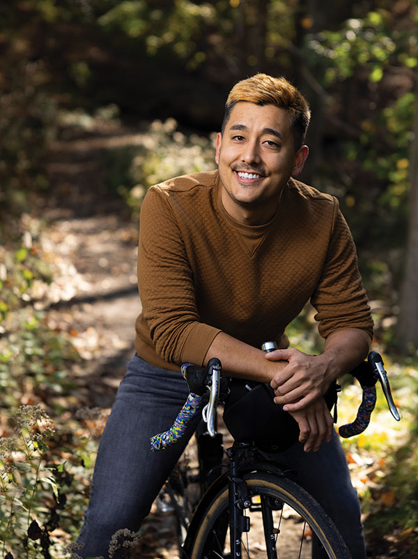 A photo of a young man in a brown shirt, sitting on a bike and smiling