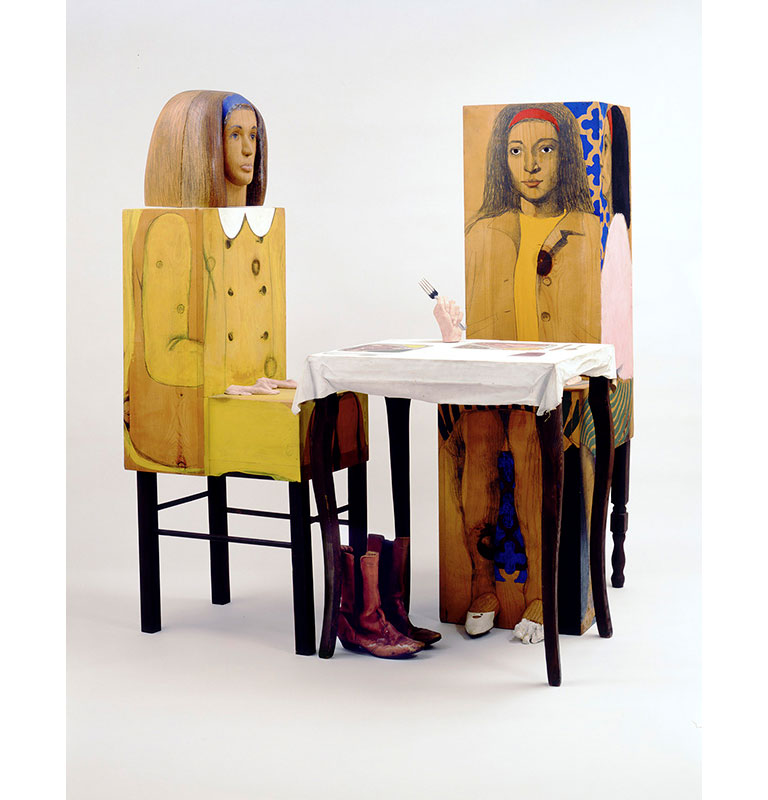 A boxy wooden sculpture of 2 women eating at a table