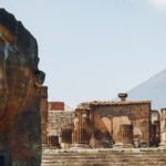 A few of a city ruins with a large sculpture of a human face in the foreground