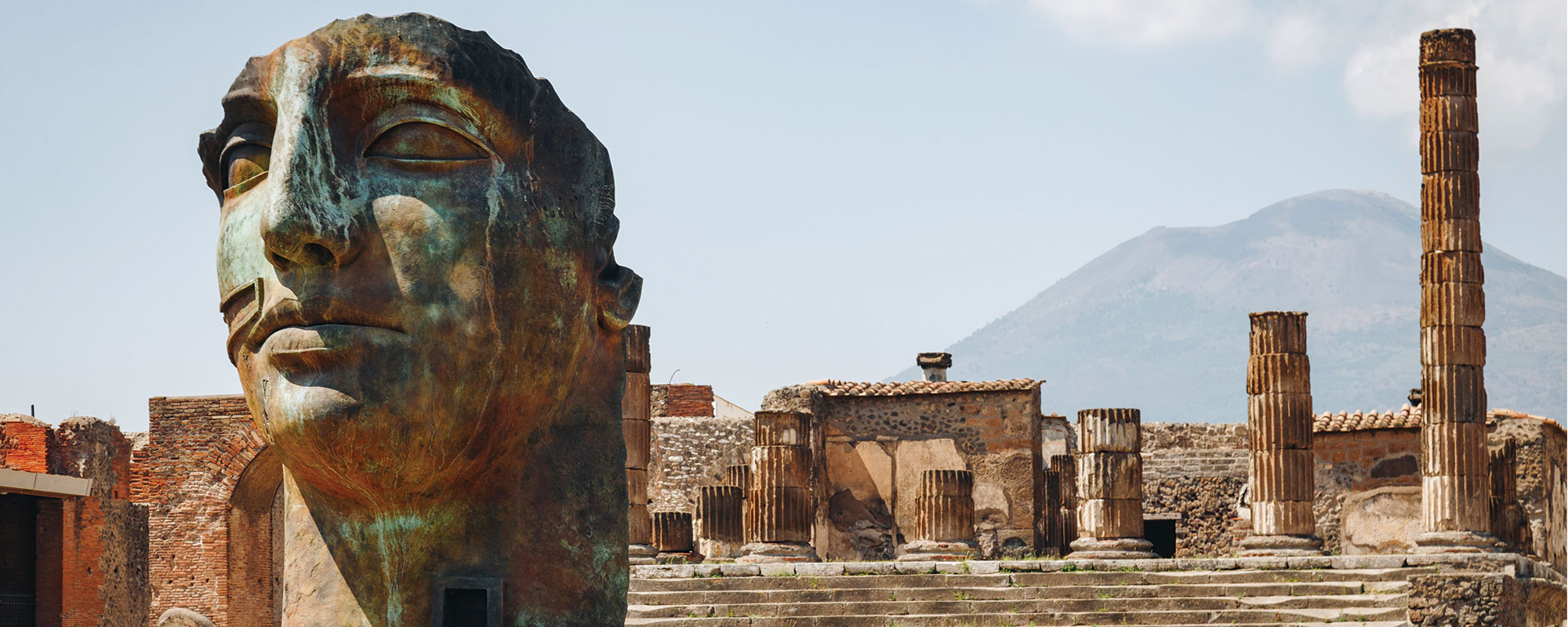 A few of a city ruins with a large sculpture of a human face in the foreground