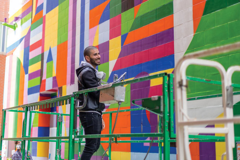 A man standing on a scaffold painting a colorful mural