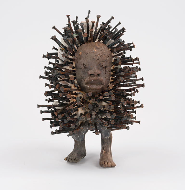 A small wooden sculpture of a figure standing and covered with protruding nails.