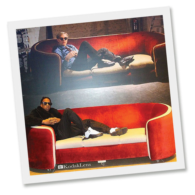 A poloaroid phot of the musicial Jay-Z sitting on a red couch, mimicking the photo on the wall above him of Andy Warhol on the same couch.