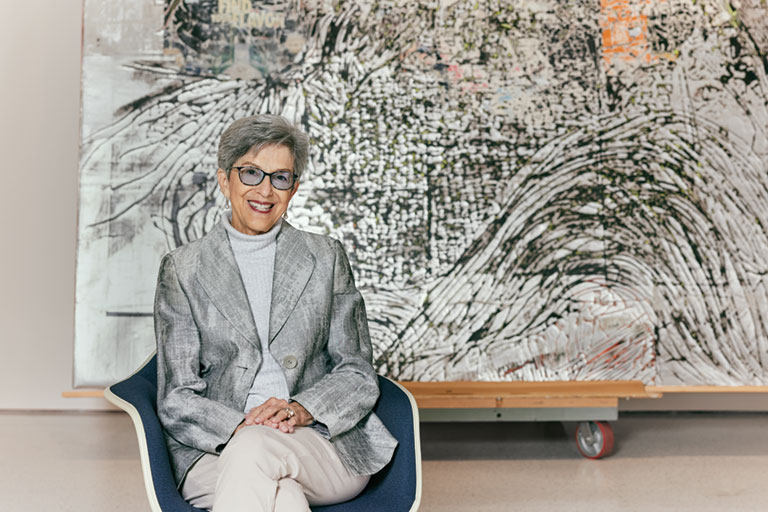 A photo of Sheila Fine seated in front of a large abstract painting.