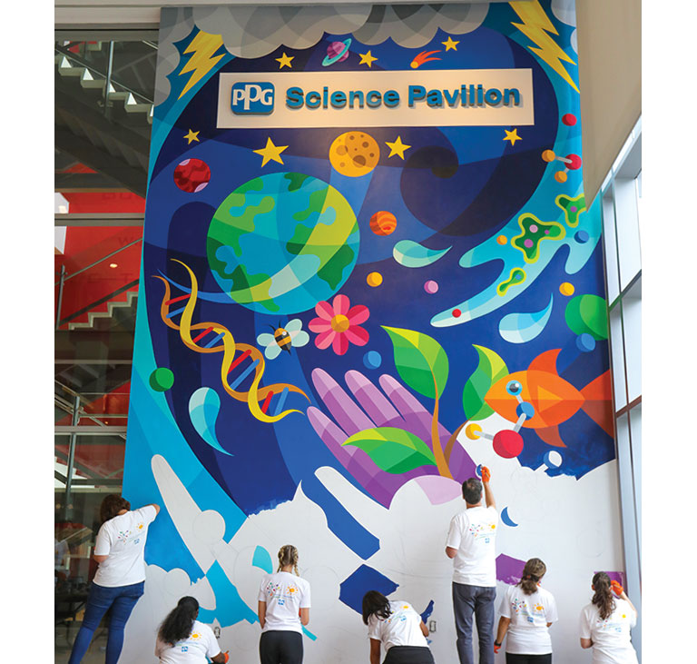 A group of people paining a colorful mural on a large panel.