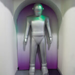 A silver robot figure stands in an archway, set against a gradient purple background, evoking a futuristic vibe.