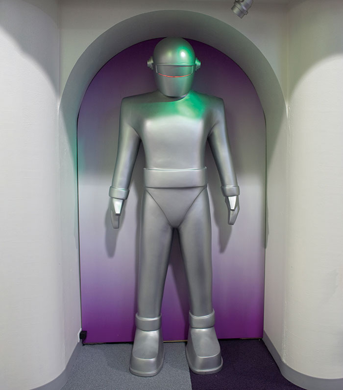 A silver robot figure stands in an archway, set against a gradient purple background, evoking a futuristic vibe.