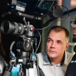 A diverse team of three people reviews footage on set. A woman with headphones, a man focused on the camera, and another wearing a headset.