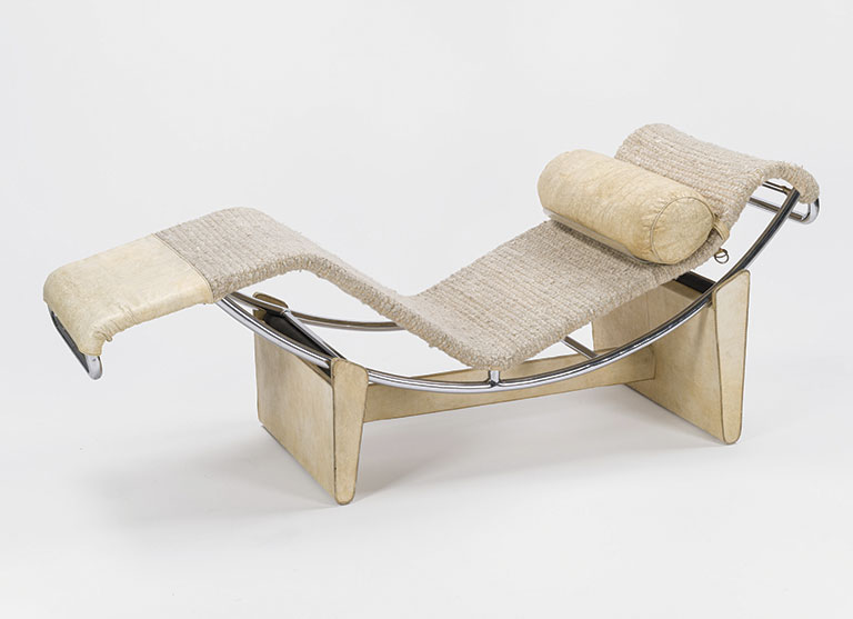 Curved, modern chaise lounge with a chrome frame, beige woven fabric, and a cylindrical pillow. The design is minimalist and elegant.