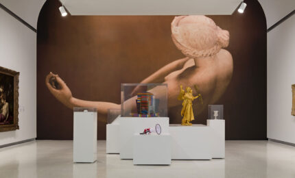 Gallery with large artwork of a reclining figure on the wall. Foreground features modern sculptures on white pedestals, including a golden figure. Traditional paintings frame the scene.